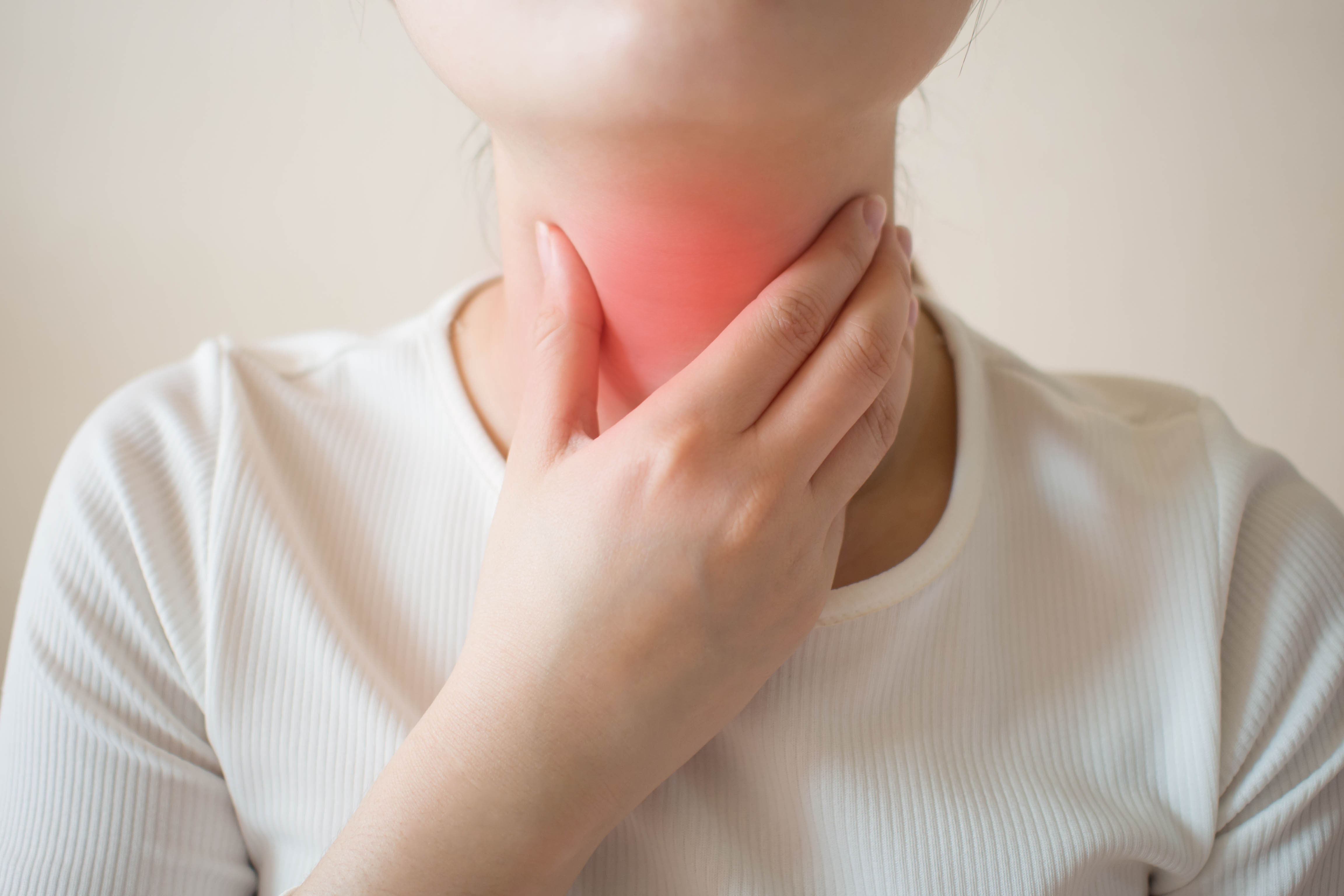 Sick women suffering from sore throat on gray background. Causes of throat pain include flu, common cold, bacterial infections, allergies, smoke, GERD or tumor. Health and medical concept. Close up.
